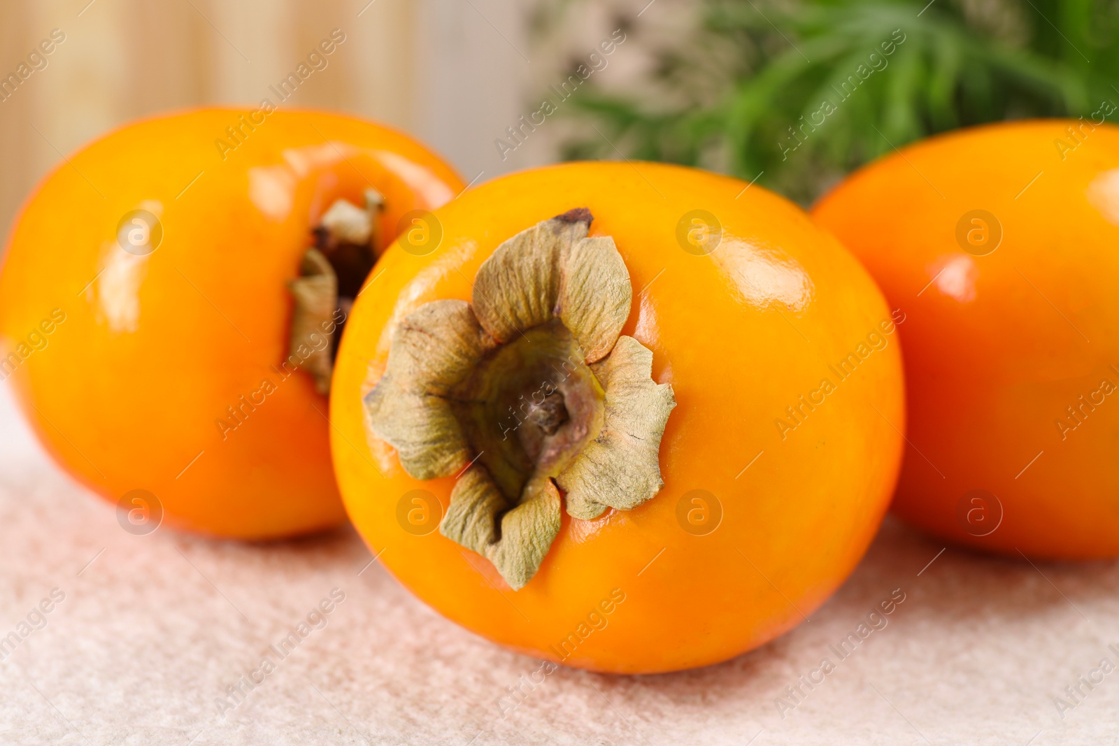 Photo of Delicious ripe persimmons on light textured table indoors, closeup