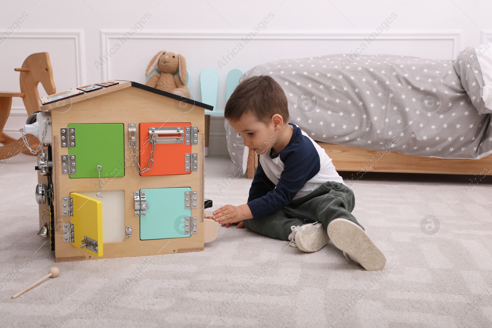 Photo of Little boy playing with busy board house on floor at home