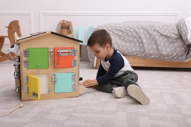 Photo of Little boy playing with busy board house on floor at home