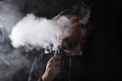 Photo of Man using electronic cigarette on black background