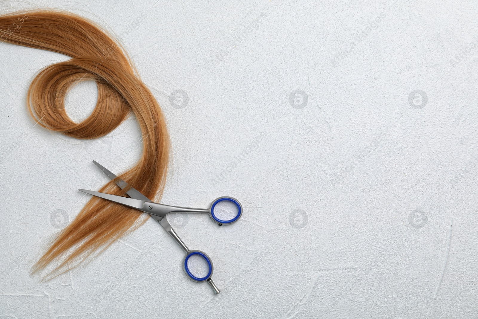 Photo of Professional hairdresser's scissors and strand of blonde hair on light background