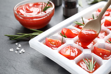Pouring sauce into ice cube tray with tomatoes and rosemary on grey table, closeup