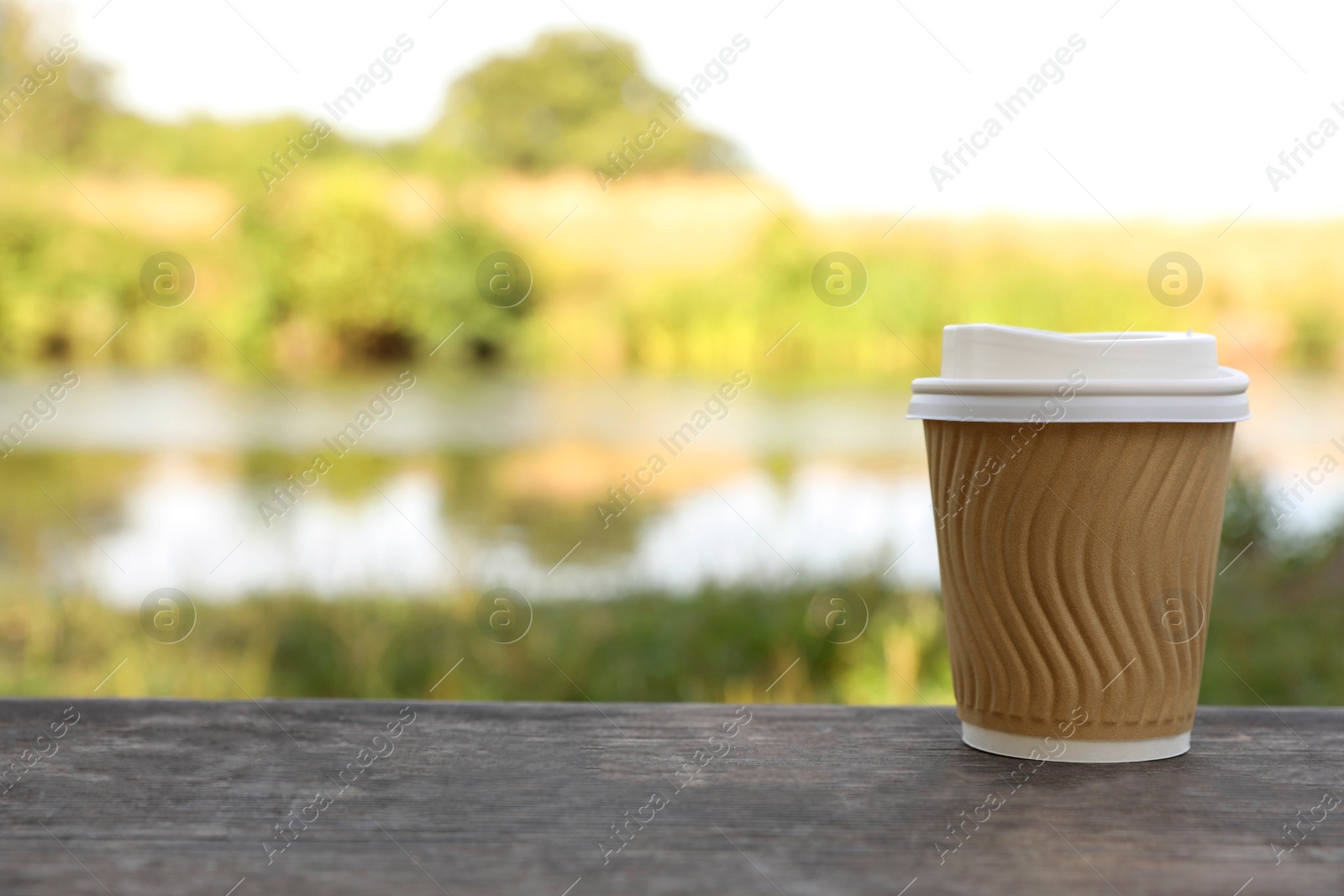 Photo of Paper cup on wooden bench outdoors, space for text. Coffee to go