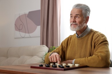 Photo of Playing checkers. Senior man thinking about next move at table in room, space for text