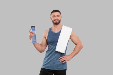 Handsome sportsman with bottle of water and white towel on grey background