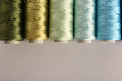 Different colorful sewing threads on light grey background, flat lay. Space for text