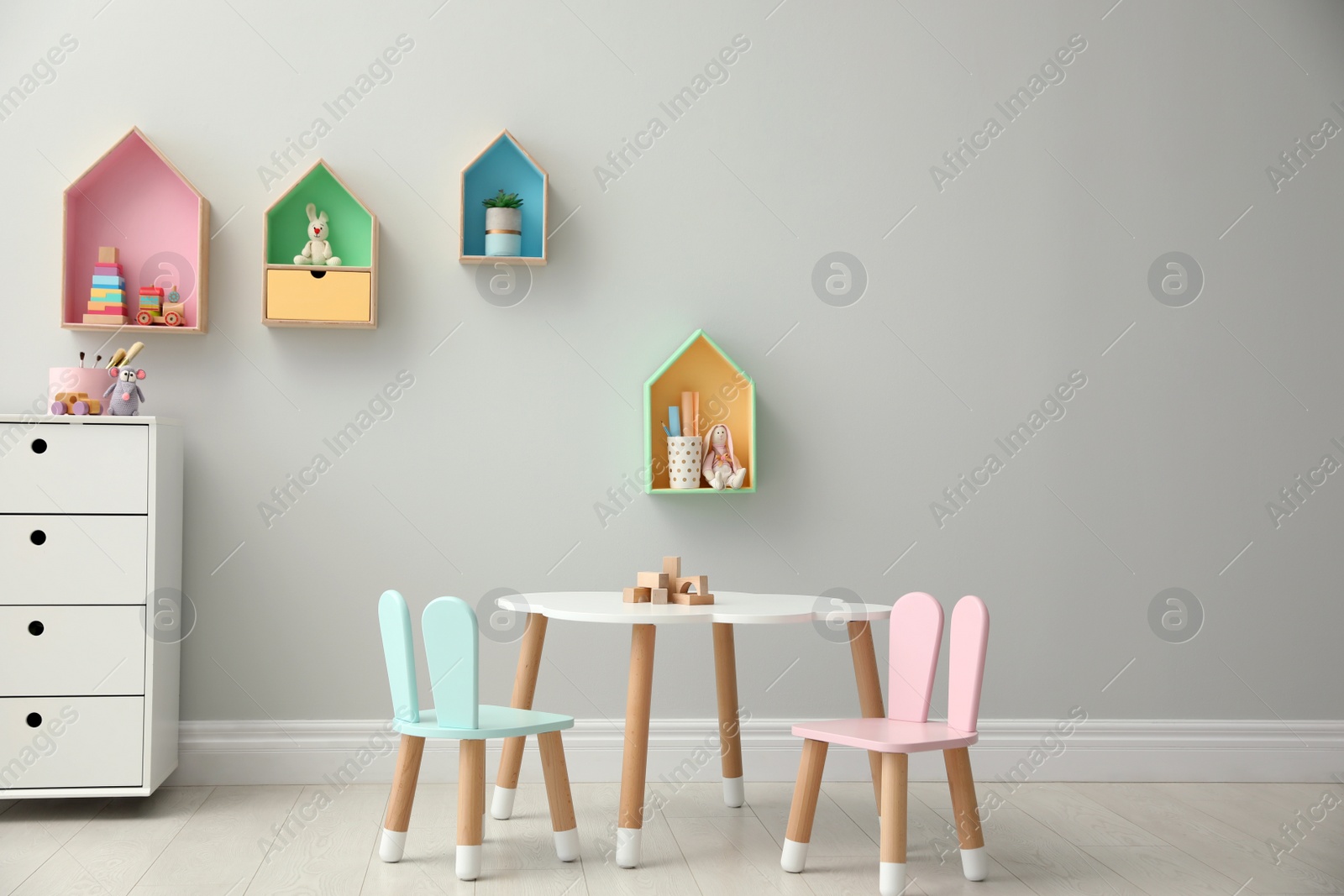 Photo of House shaped shelves and little table with chairs in children's room. Interior design