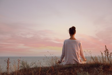 Photo of Woman meditating near sea, back view. Space for text