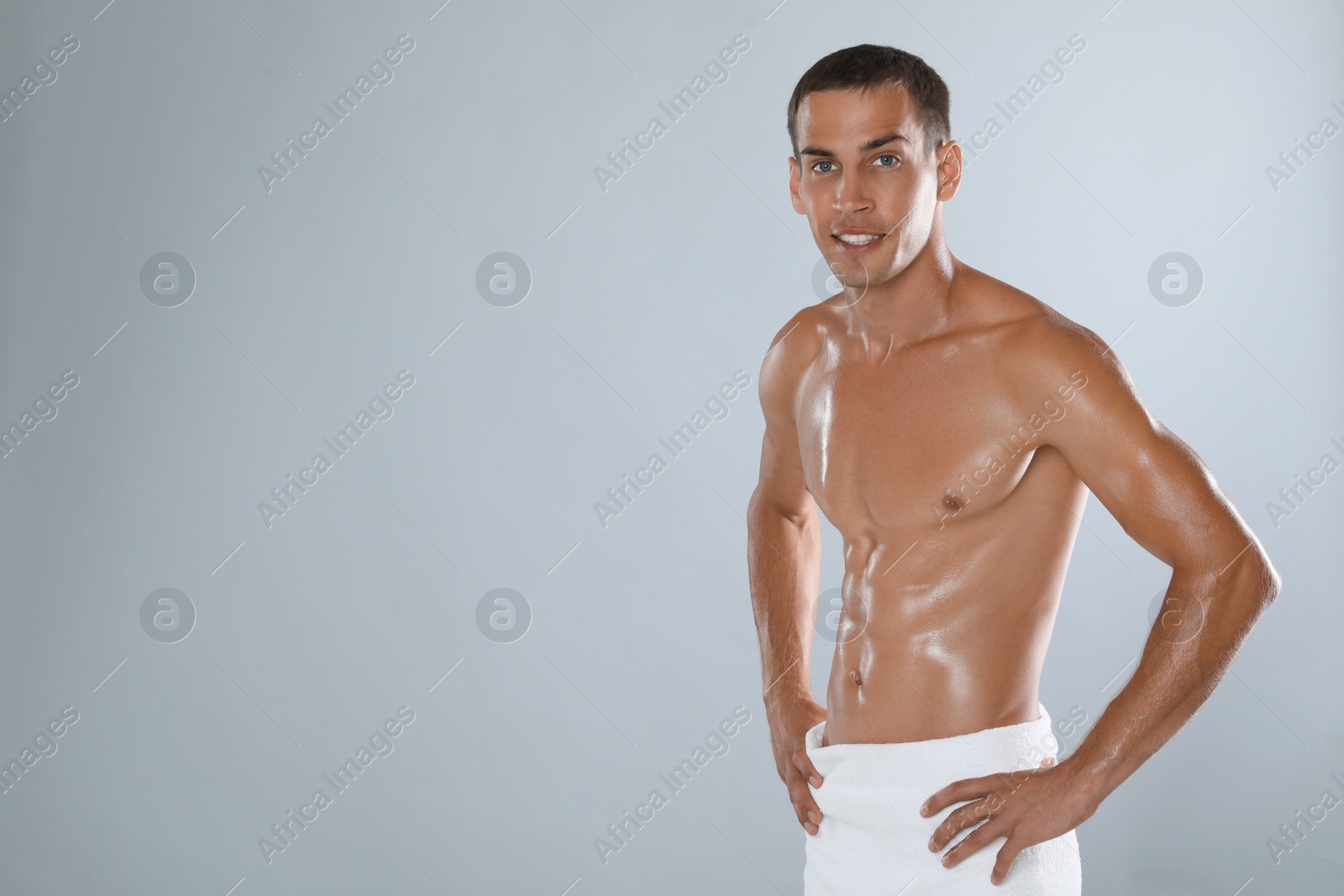 Photo of Handsome shirtless man with slim body and towel wrapped around his hips on grey background. Space for text