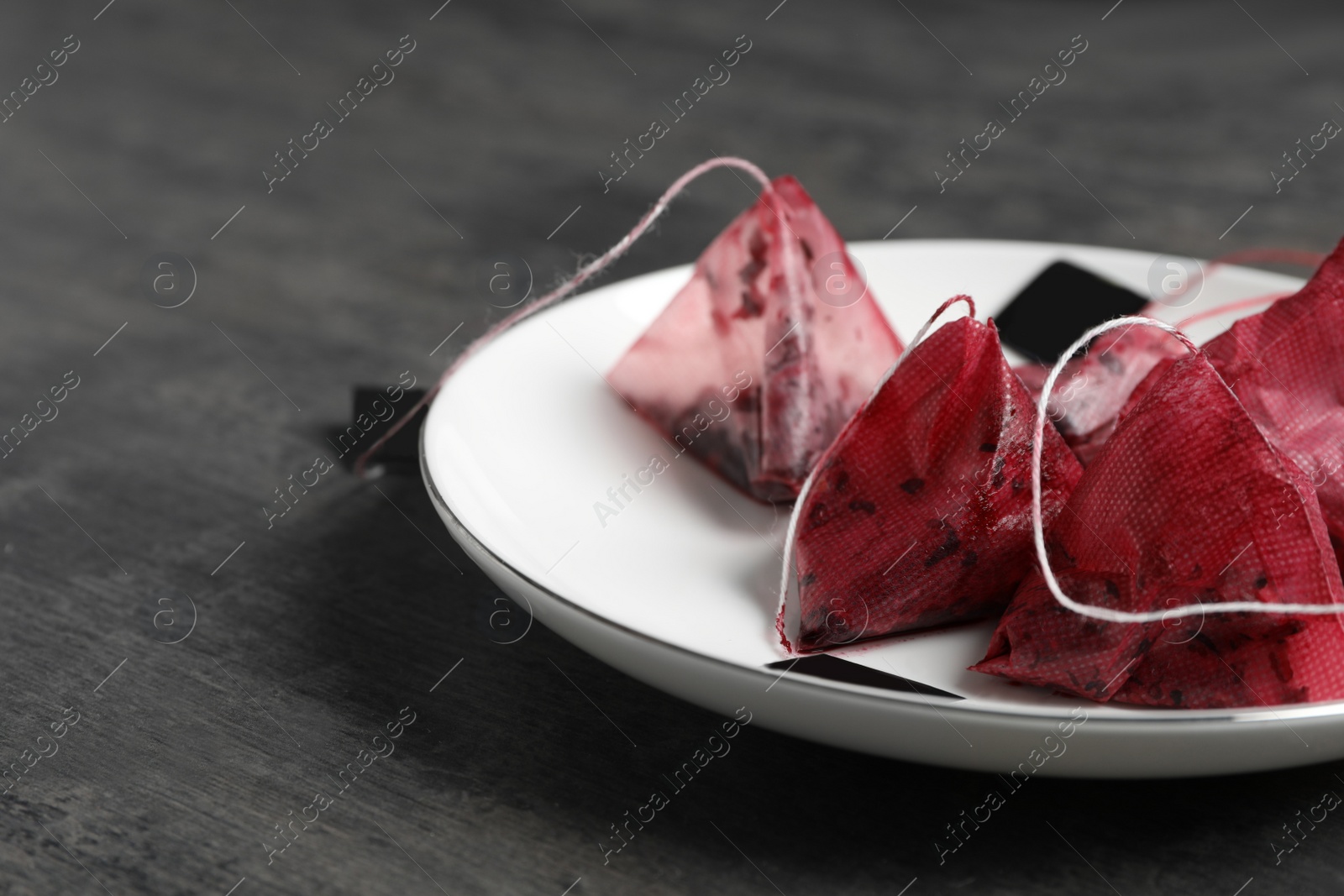 Photo of Saucer with used pyramid tea bags on grey table, closeup. Space for text