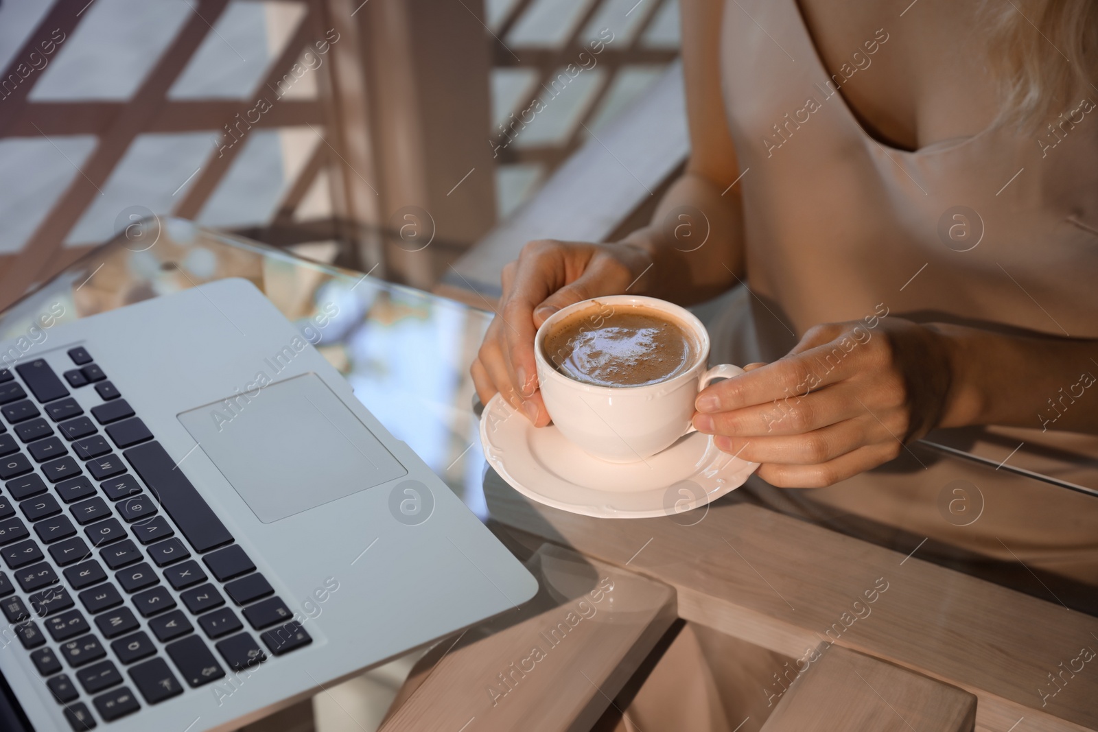 Photo of Woman with cup of coffee and laptop on cafe terrace in morning, closeup