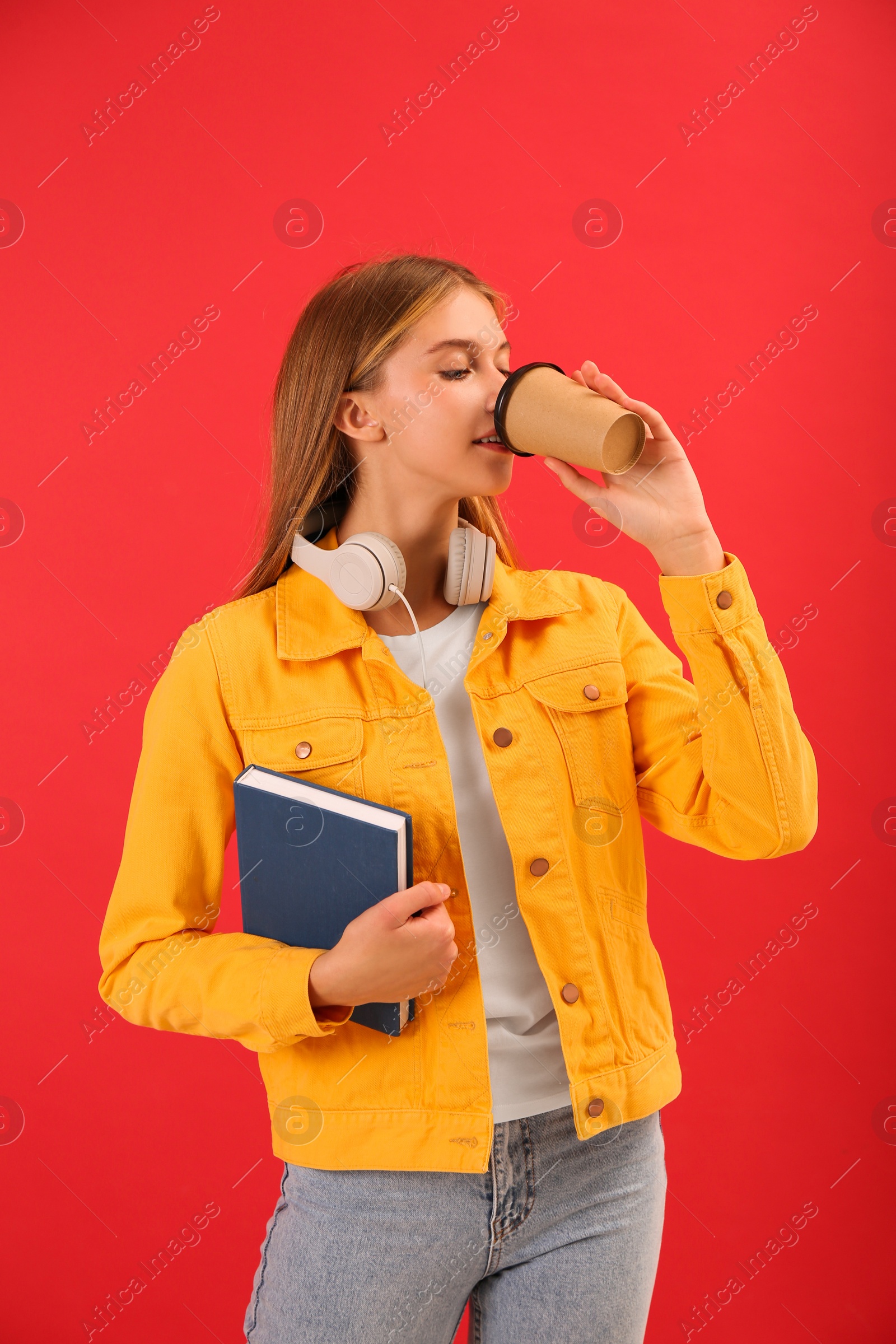 Photo of Teenage student with book drinking coffee on red background