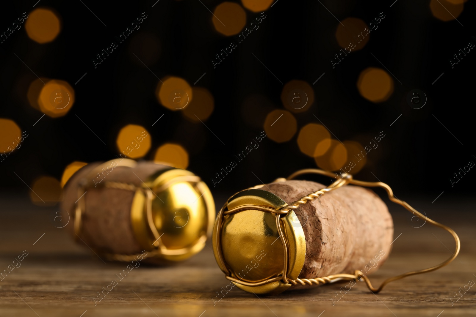 Photo of Corks of sparkling wine and muselet caps on wooden table against blurred festive lights, closeup. Bokeh effect