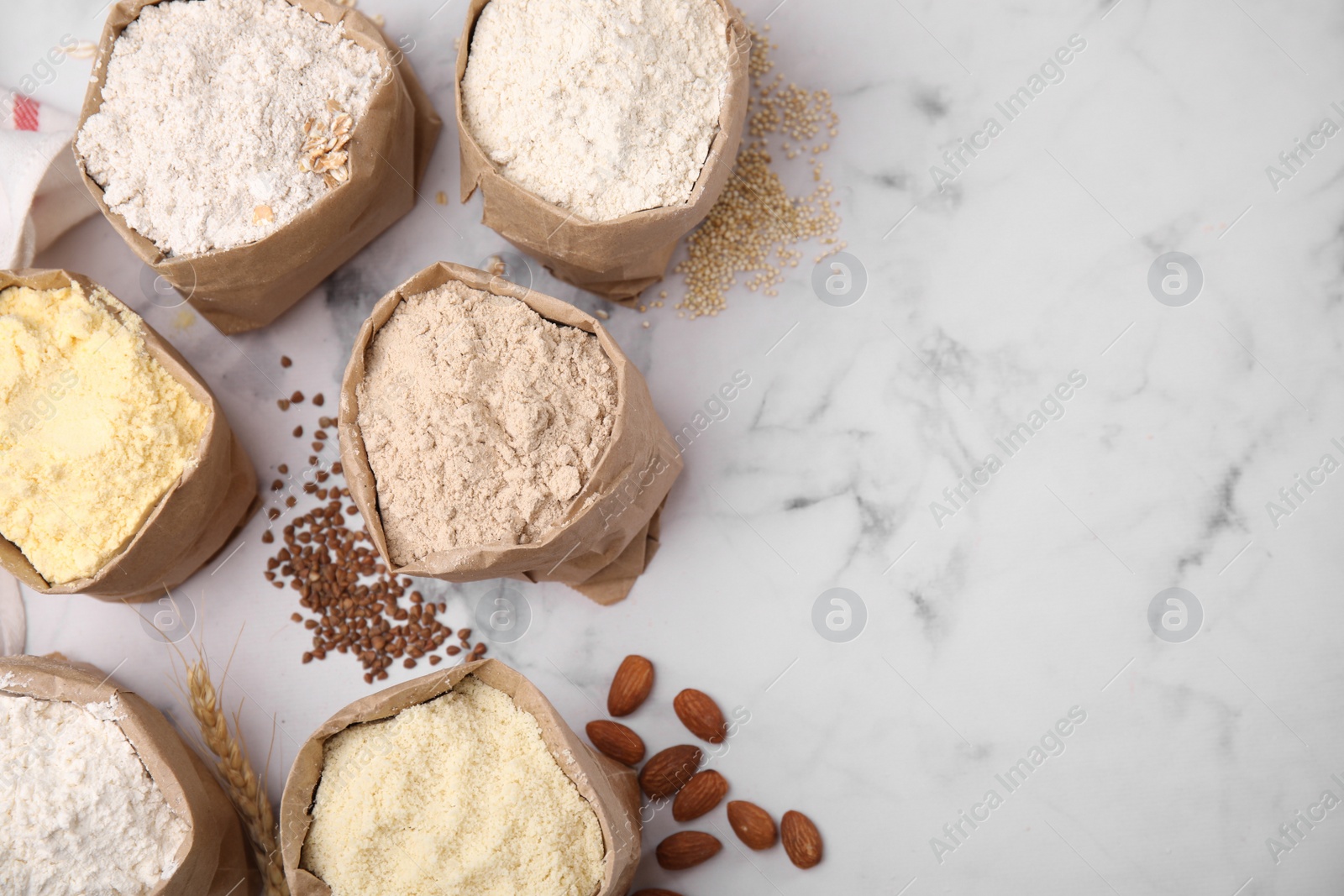 Photo of Paper bags with different types of flour and ingredients on white marble table, flat lay. Space for text