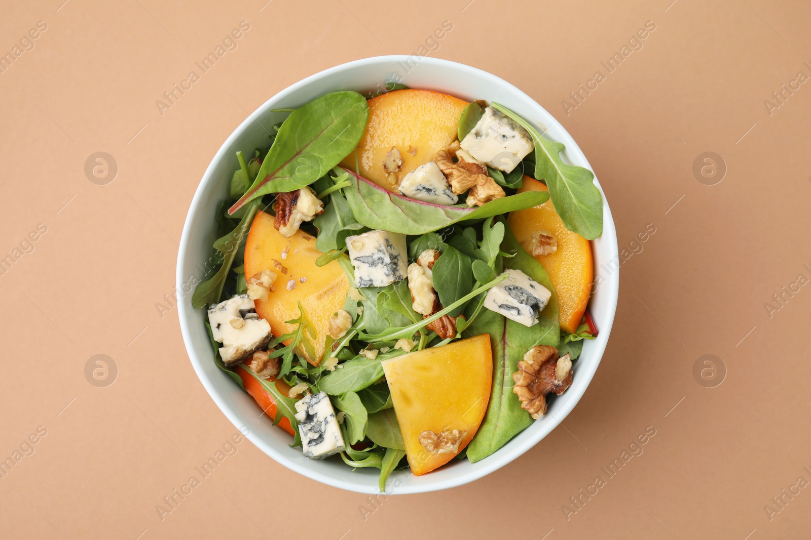 Photo of Tasty salad with persimmon, blue cheese and walnuts served on light brown background, top view
