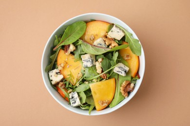 Tasty salad with persimmon, blue cheese and walnuts served on light brown background, top view