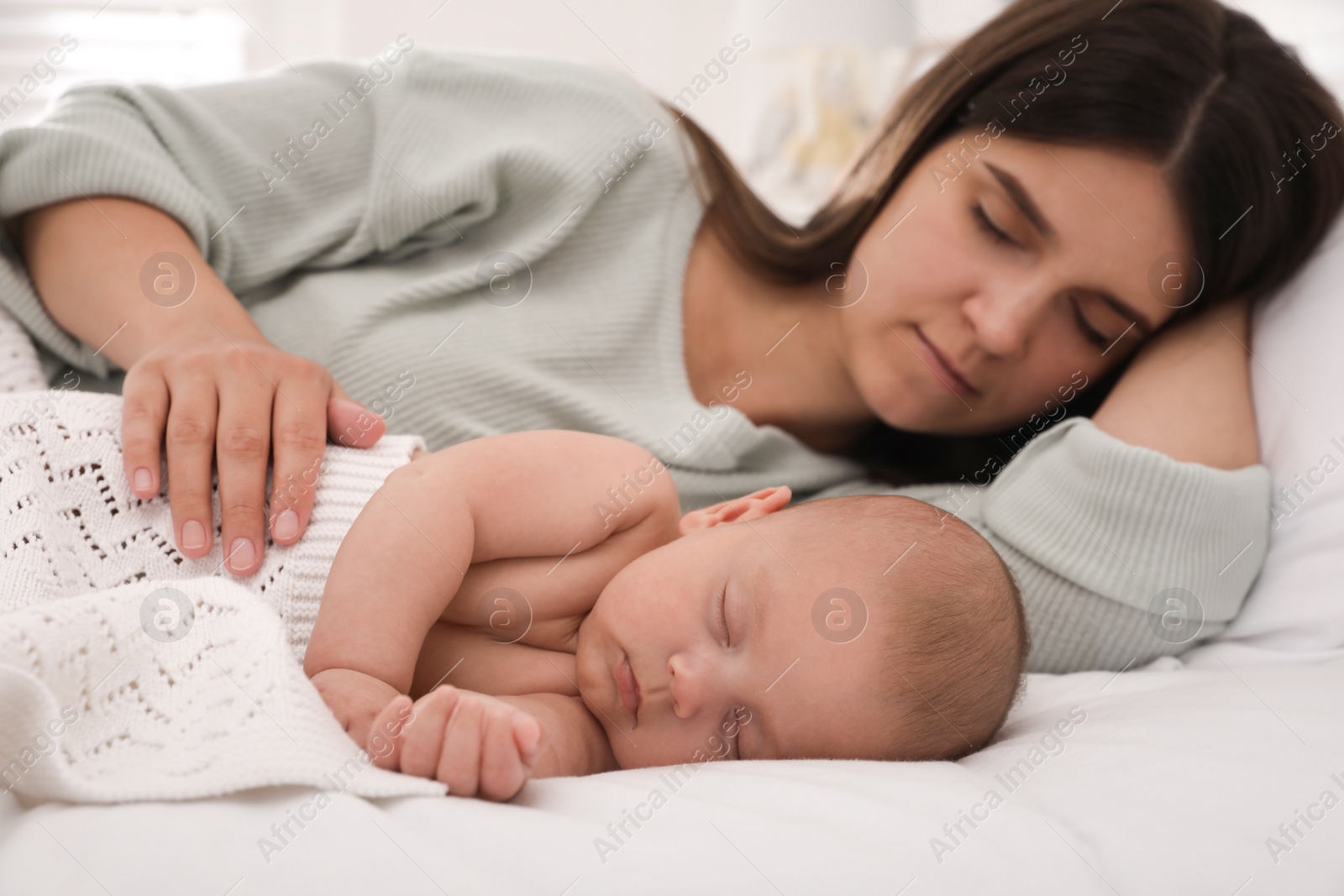 Photo of Young mother resting near her sleeping baby on bed at home