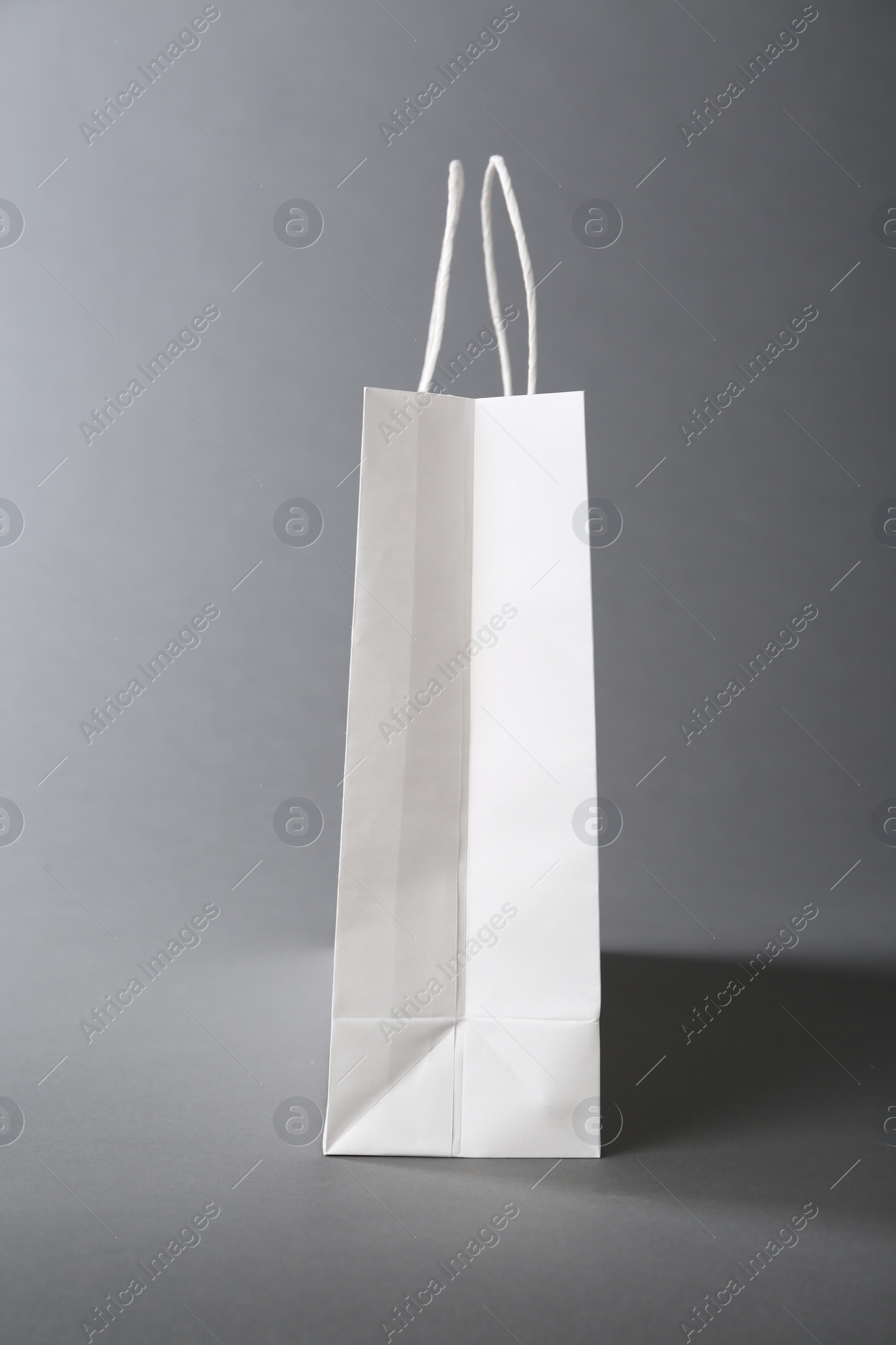 Photo of One white paper bag on grey background. Mockup for design