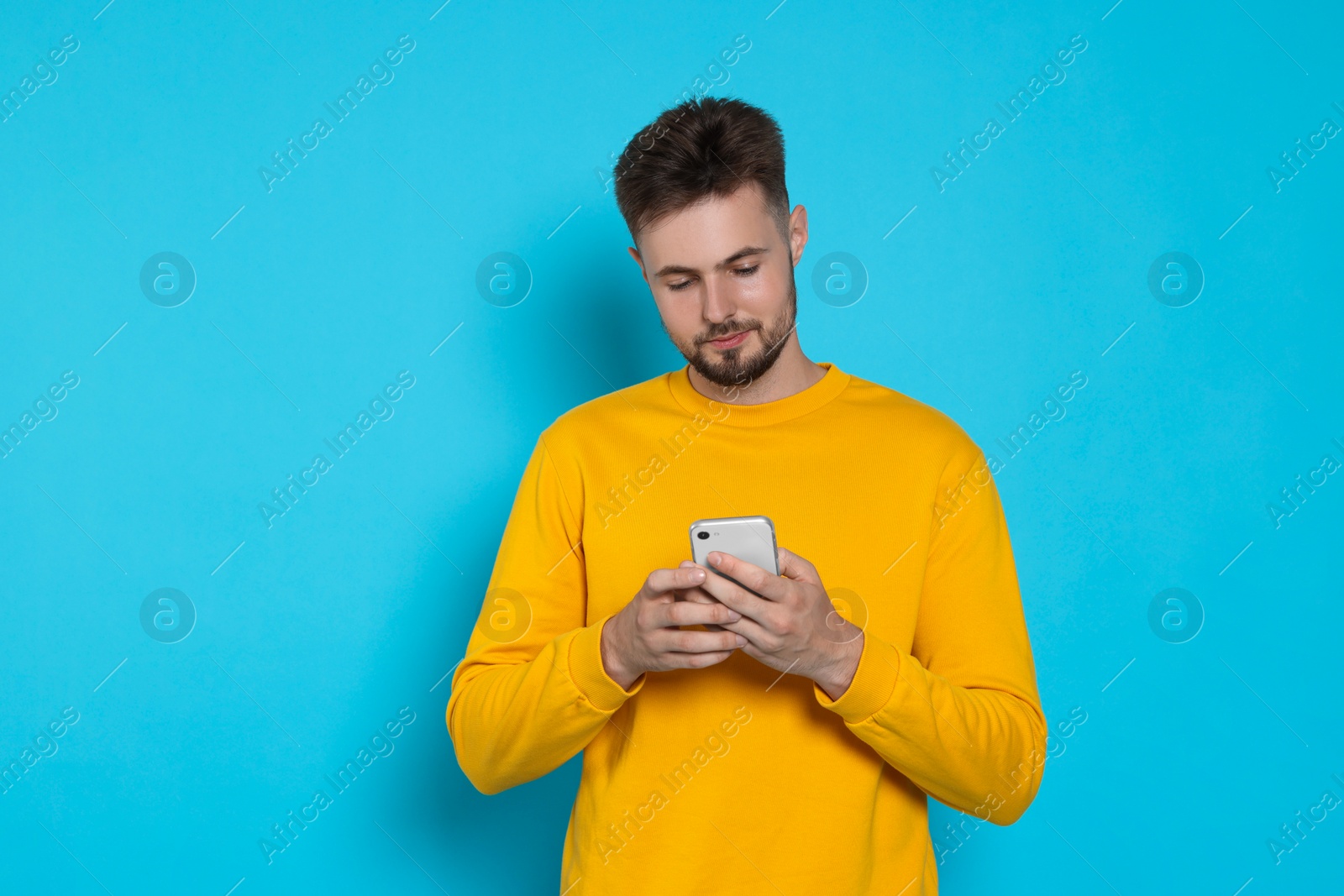 Photo of Handsome man in yellow sweatshirt with phone on light blue background