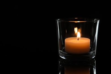 Photo of Wax candle burning on table in darkness, closeup