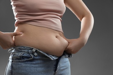 Photo of Woman touching belly fat on grey background, closeup. Overweight problem