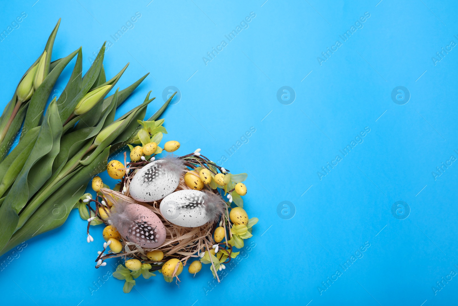 Photo of Flat lay composition with flowers and eggs on light blue background, space for text. Easter celebration