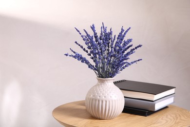 Photo of Bouquet of beautiful preserved lavender flowers and notebooks on wooden table near beige wall, space for text