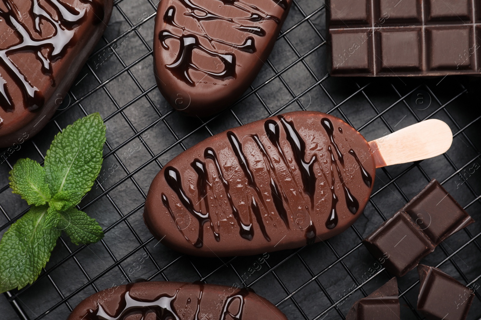 Photo of Delicious glazed ice cream bars, chocolate and mint on black table, flat lay