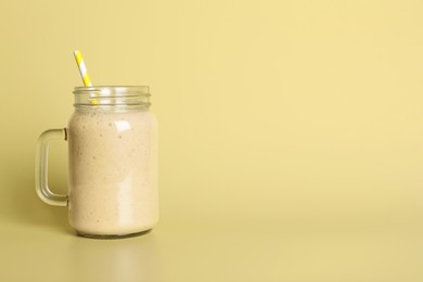 Photo of Mason jar of tasty smoothie with straw on beige background. Space for text