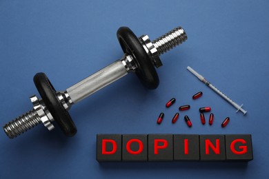 Photo of Black wooden cubes with word Doping, dumbbell and drugs on blue background, flat lay