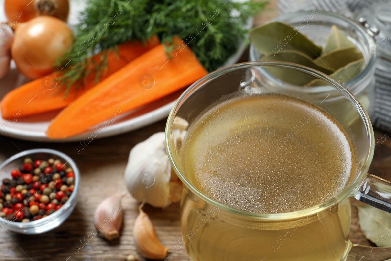 Photo of Hot delicious bouillon in glass cup and ingredients on table, closeup