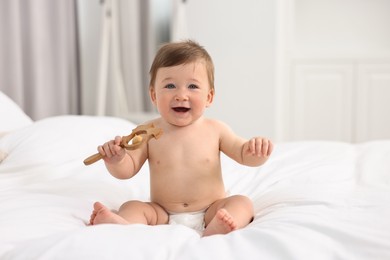 Cute baby boy with wooden rattle on bed at home