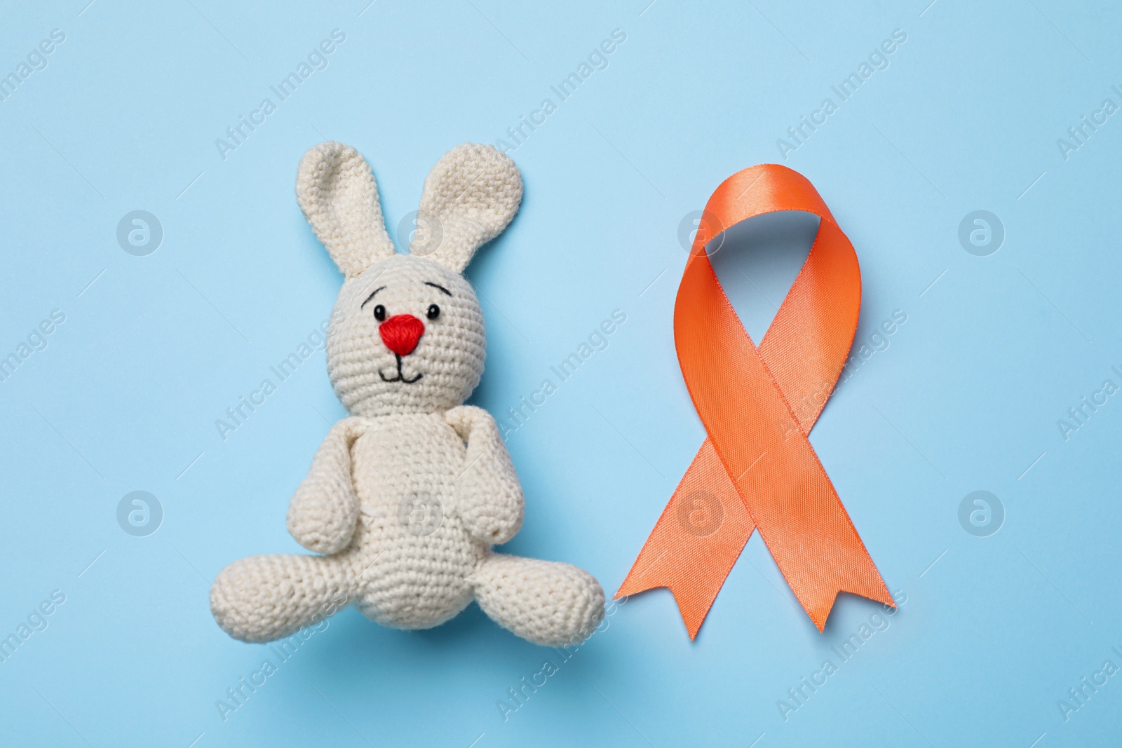Photo of Orange ribbon and toy bunny on light blue background, flat lay. Multiple sclerosis awareness