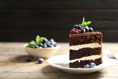 Photo of Plate with slice of chocolate sponge berry cake on wooden table