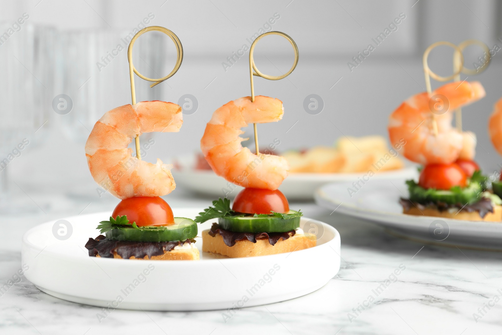 Photo of Tasty canapes with shrimps, cucumber, greens and tomatoes on white marble table, closeup