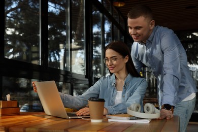 Photo of Young students with laptop studying at table in cafe