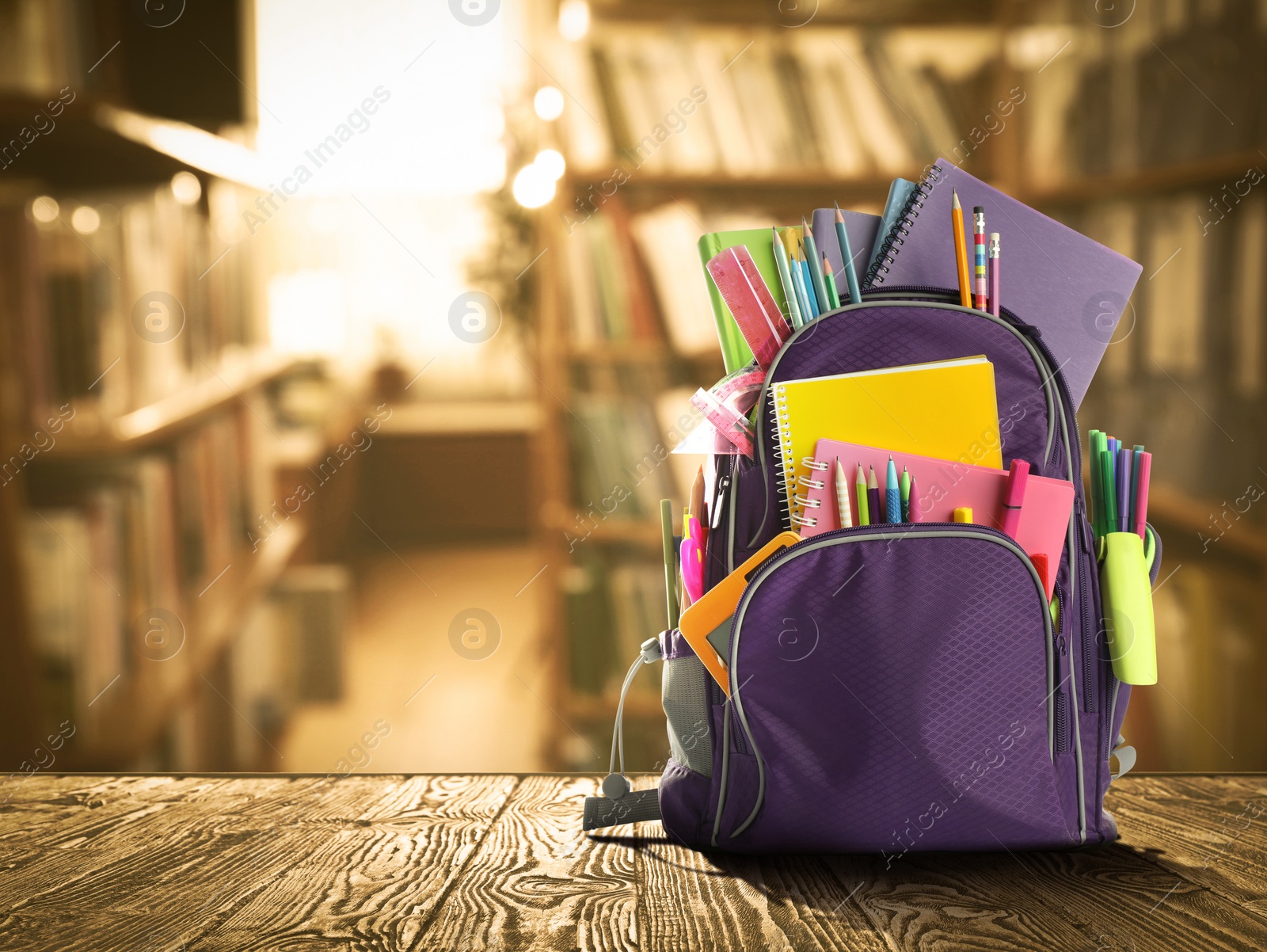 Image of Backpack with school stationery on wooden table in library, space for text