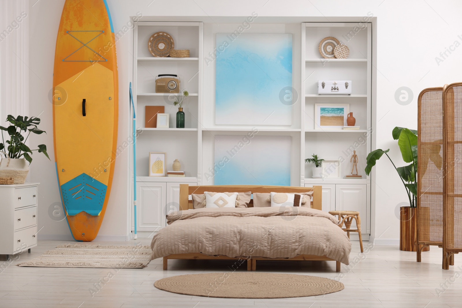 Photo of SUP board, bed and furniture in room. Interior design