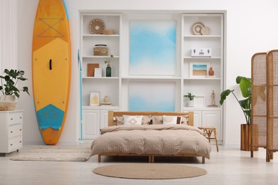 Photo of SUP board, bed and furniture in room. Interior design