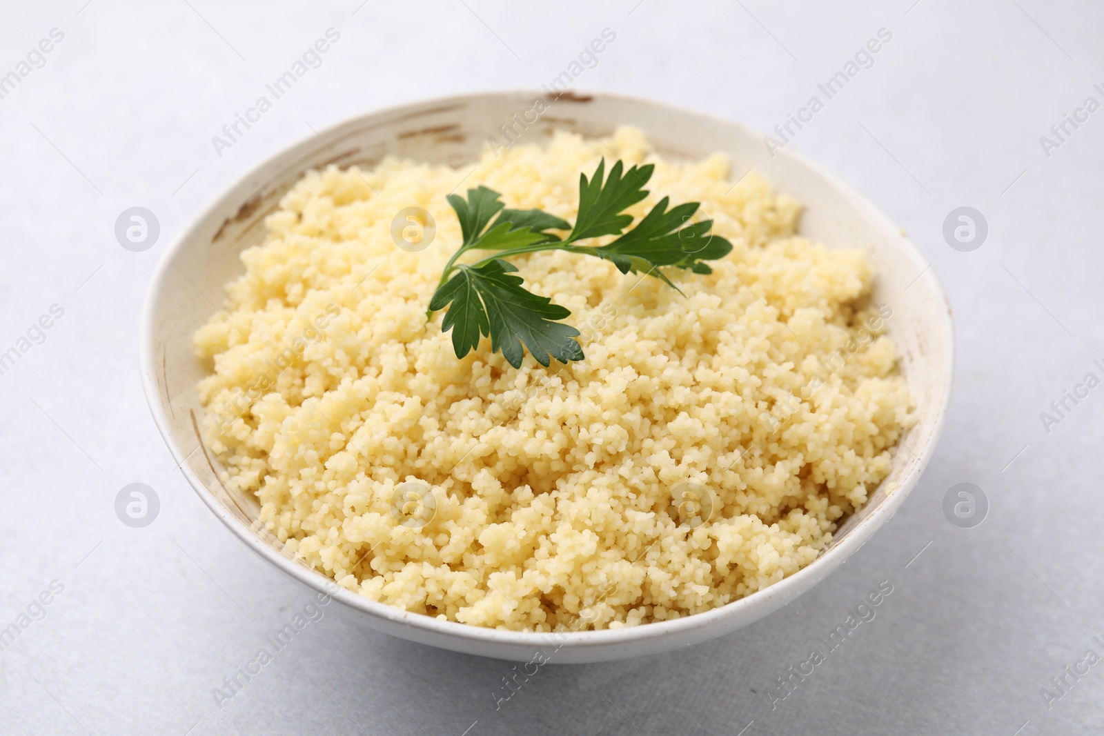 Photo of Tasty couscous and fresh parsley in bowl on light grey table, closeup