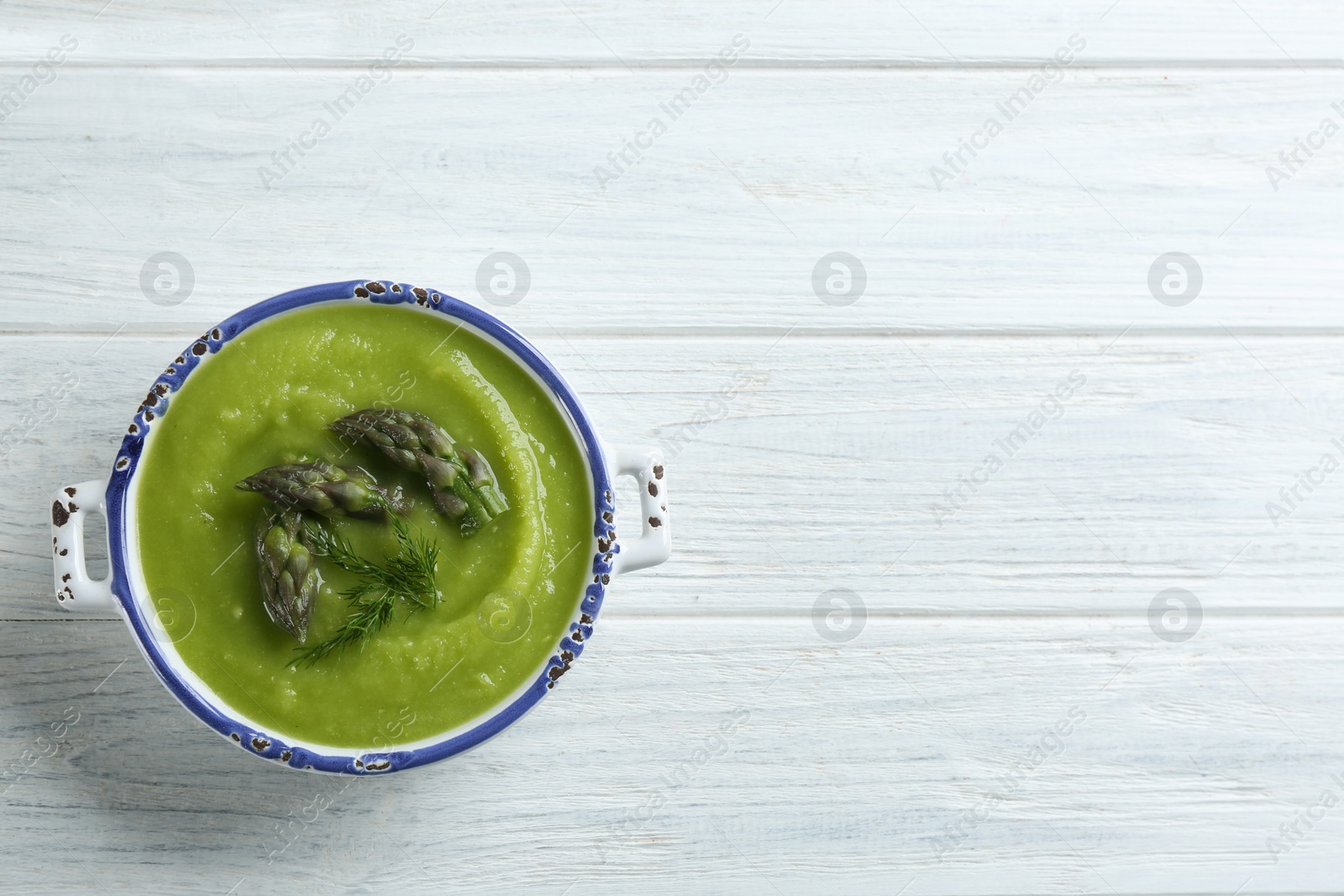 Photo of Delicious asparagus soup in bowl on white wooden table, top view. Space for text