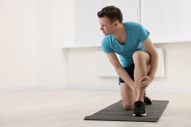 Photo of Man suffering from leg pain on mat indoors. Space for text