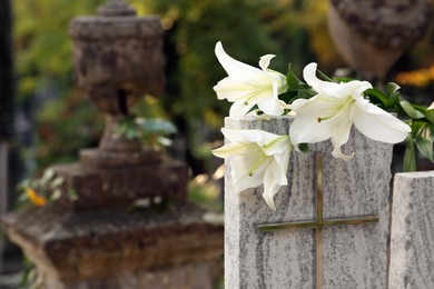 Photo of White lilies on granite tombstone outdoors, space for text. Funeral ceremony