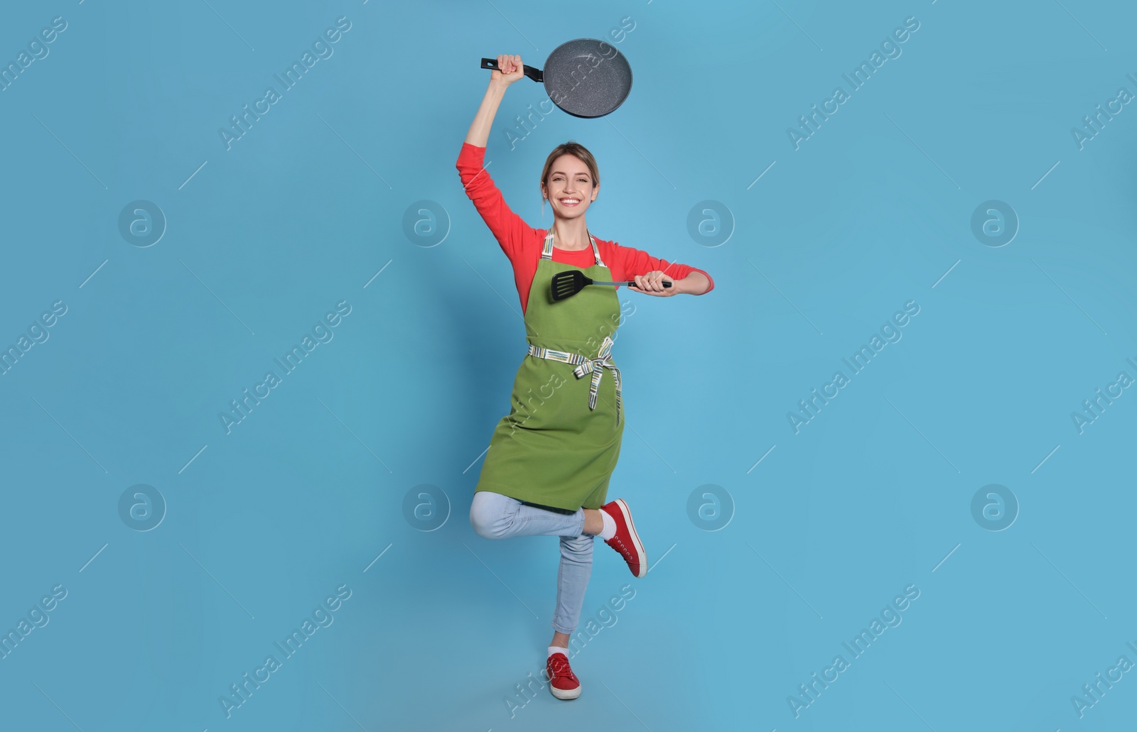 Photo of Young housewife meditating with frying pan and spatula on light blue background