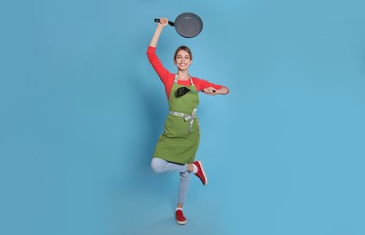 Photo of Young housewife meditating with frying pan and spatula on light blue background
