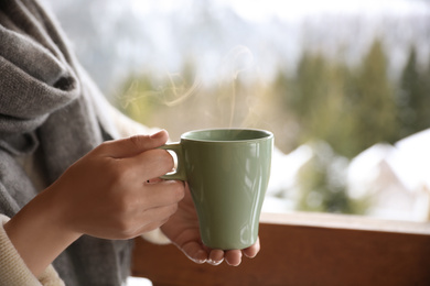 Photo of Woman with cup of tasty coffee outdoors on winter morning, closeup