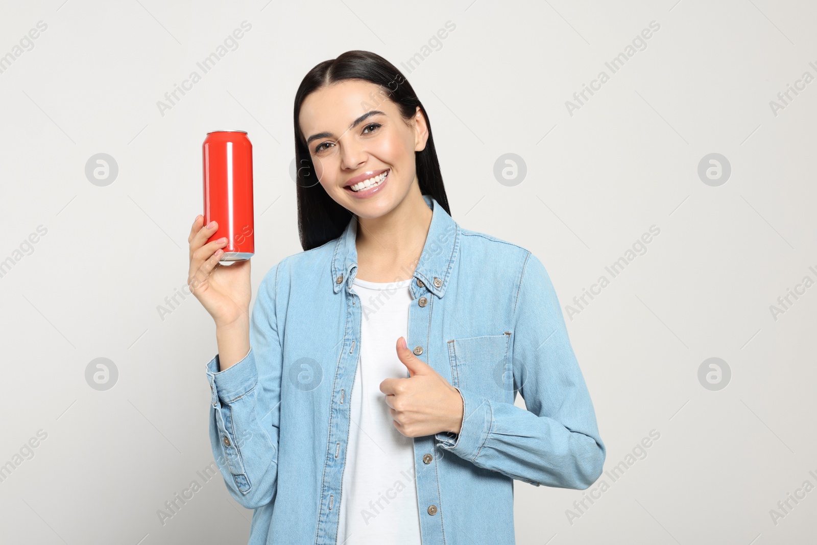 Photo of Beautiful happy woman holding red beverage can and showing thumbs up on light grey background