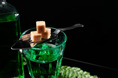 Absinthe in glass, brown sugar and spoon on table against black background, space for text. Alcoholic drink