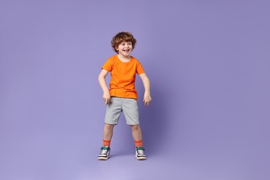 Photo of Happy little boy dancing on violet background