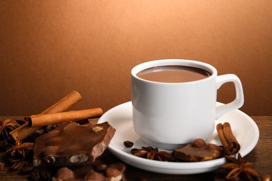 Photo of Cup of delicious hot chocolate, spices and coffee beans on wooden table